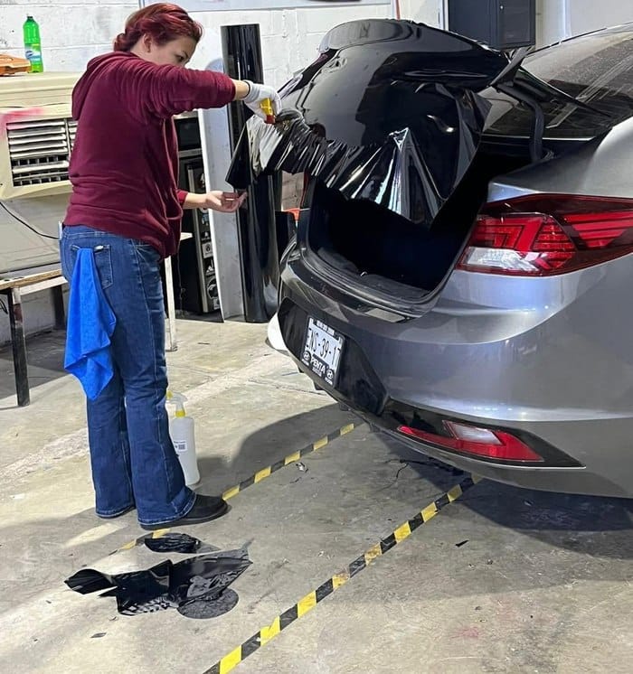 Alumna instalando wrap negro en la cajuela de un sedán